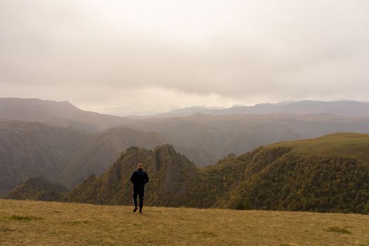 阴天，一名面目全非的男子走在山峰环绕的草地上，留下背影