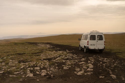 Old white van parked on dry land in hilly terrain in steppe in daytime