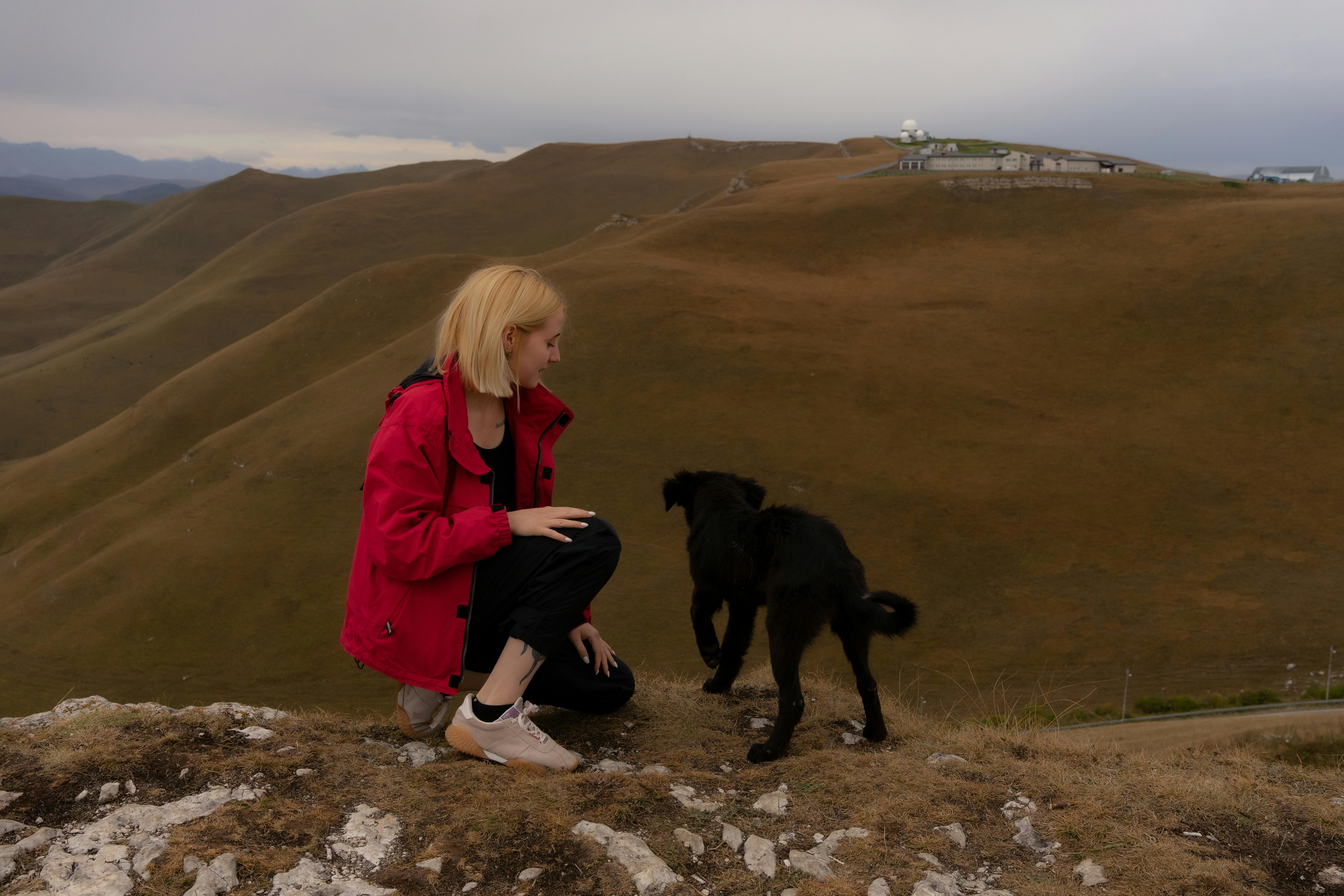 Female squatting down near dog against mountains