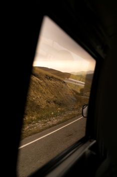 Asphalt roadway among wild fields and hills under cloudy sky through car window