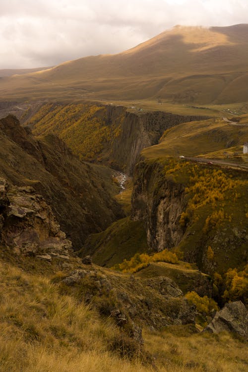 Amazing view of rough mountain formation with grass and rocks near mountains in overcast weather