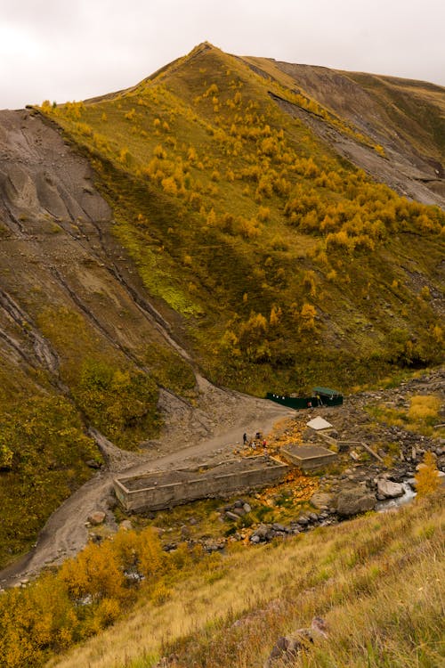 Picturesque view of grassy terrain with destruct buildings near slope and mountain ridge