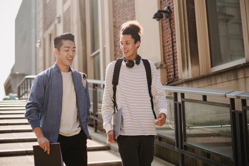 Free Smiling multiracial classmates with folder and laptop wearing casual clothes walking together and discussing studies Stock Photo