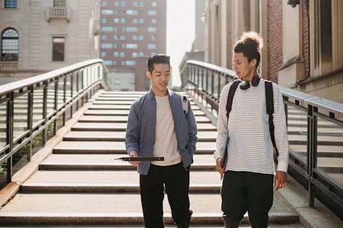 Free Diverse classmates wearing casual clothes walking on stairway of university building and discussing studying Stock Photo