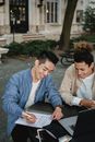 两名大学生面带微笑，全神贯注地在户外学习和讨论笔记