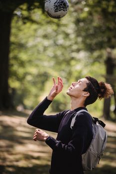 Side view of attentive man with backpack playing with ball in park with tall trees
