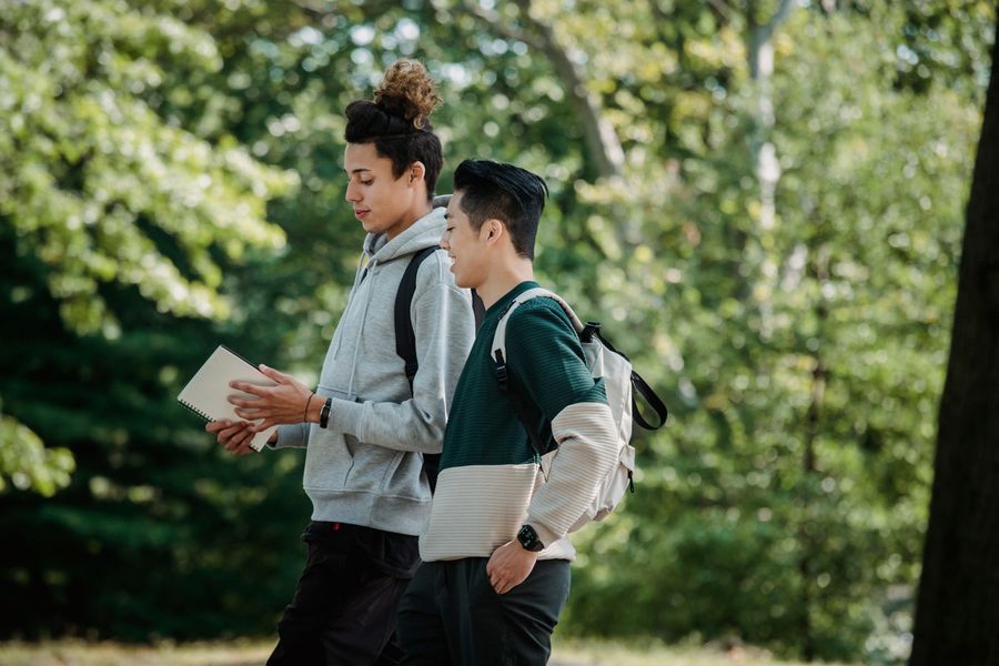 Multi-ethnic classmates with backpacks and notebooks walking through a university park
