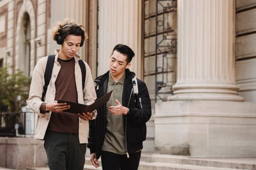 Free Concentrated multiracial male classmates reading document in folder and talking about studies near university building Stock Photo