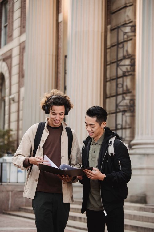 Free Smiling multiracial classmates in casual wear discussing report together standing near  historic university building Stock Photo