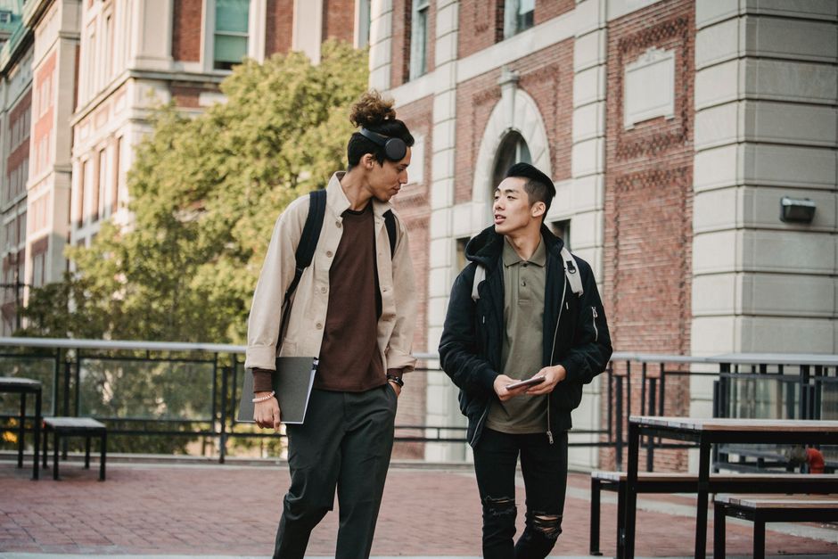 Young multiethnic men in casual informal outfit and stylish haircuts promenading and discussing new project while looking at each other Young multiethnic men in casual informal outfit and stylish haircuts promenading and discussing new project while looking at each other
