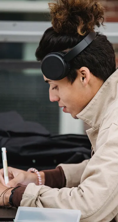 Young man with headphones taking notes while studying on laptop