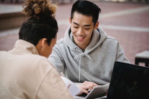 Free Cheerful diverse students surfing internet and smiling while using tablet at table on blurred background of street Stock Photo