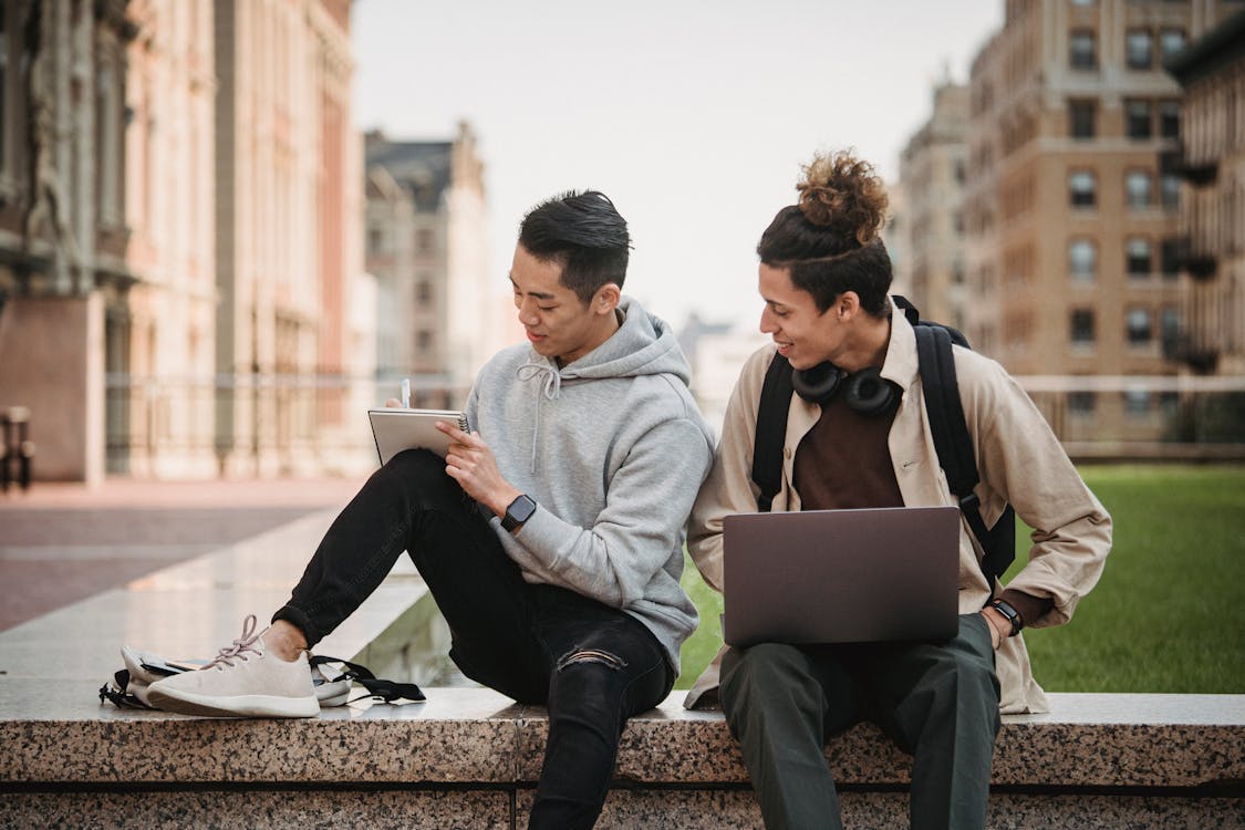 Free Man and Woman Sitting on Concrete Bench Using Laptop Computers Stock Photo