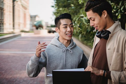 Multiethnic male students standing with folder and talking outdoors