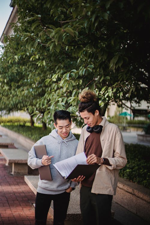 Multiracial guys standing with folder and netbook in street