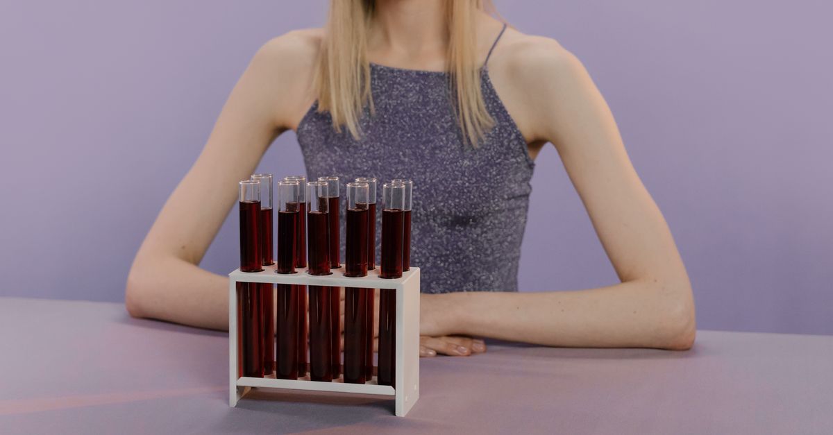 A woman sits with a rack of test tubes filled with red liquid on a table in a lab-like environment. - Evidence evidence guide for astaxanthin skin photoaging meta-analysis