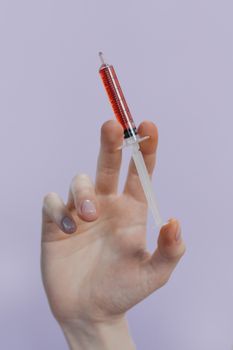 特写镜头中，一只手拿着一个充满红色液体的注射器，背景是浅紫色