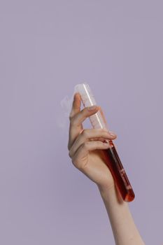 紫色背景下，一只握着装有红色液体试管的手的特写，象征着科学或实验