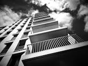 现代高层建筑外观呈现戏剧性的黑白景观，阳台和玻璃板映衬着多云的天空