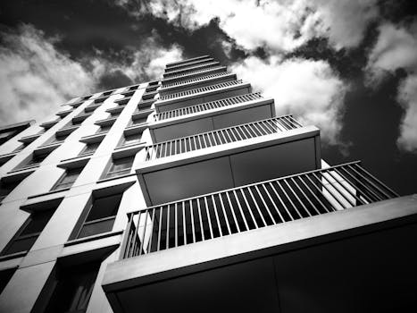 现代高层建筑外观呈现戏剧性的黑白景观，阳台和玻璃板映衬着多云的天空