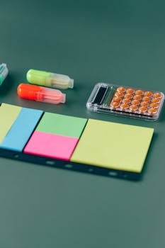Assorted office supplies including sticky notes and highlighters on a green background.