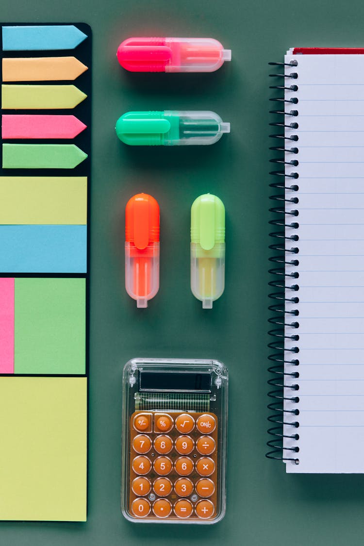 Highlighters And Calculator Beside A Spiral Notebook