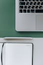 Silver Laptop on Green Surface Beside a Notebook and Pen