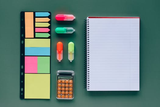 Top view of vibrant office supplies on a green background, including notebook and calculator.