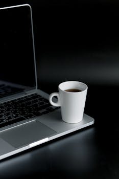 在时尚现代的工作空间里，深色办公桌上摆放着一台笔记本电脑和一杯热咖啡