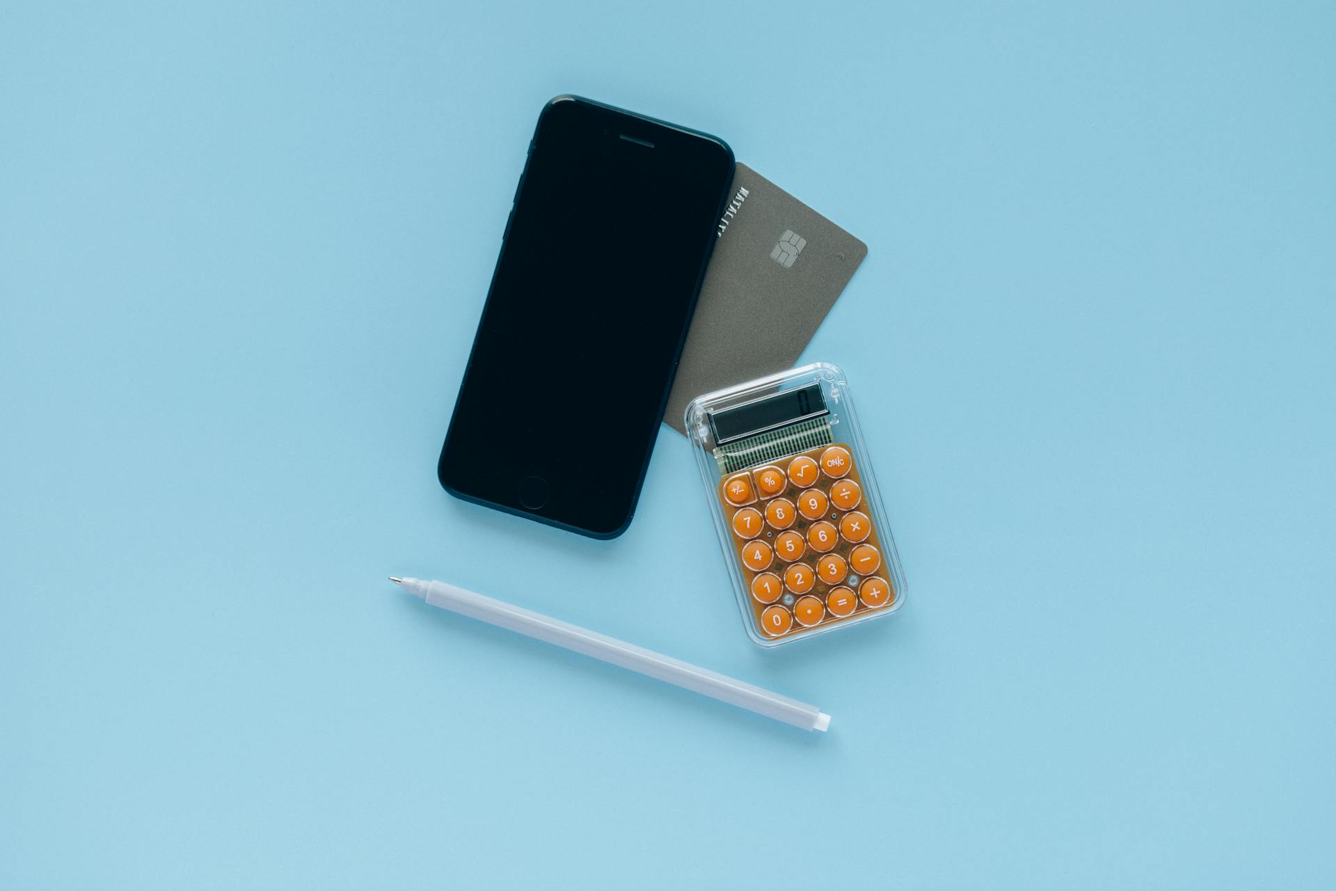 A modern flat lay of a smartphone, credit card, and calculator on a blue background.