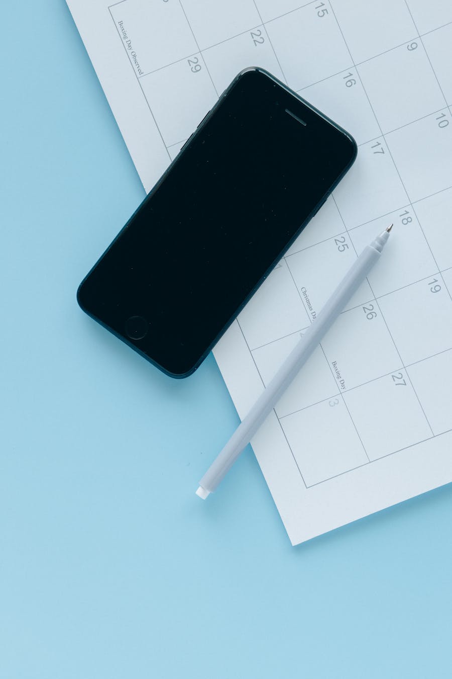 A smartphone and pen on a calendar page creating a sleek, minimalist flat lay.