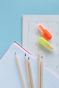 Overhead shot of calendar, notebook, wooden pencils, and highlighters on a blue background.