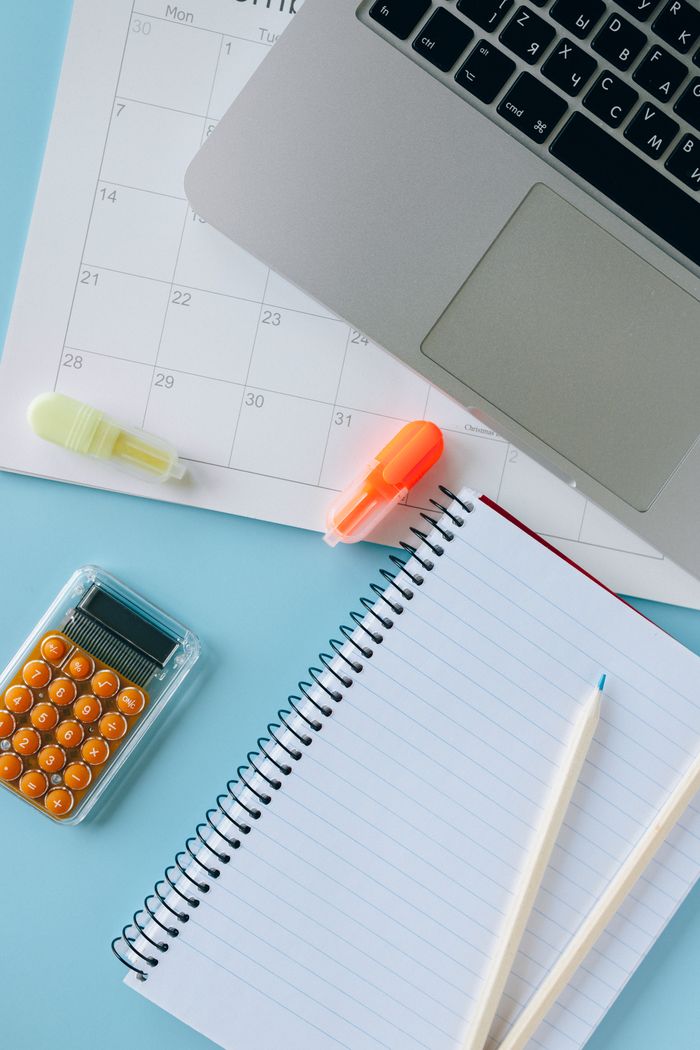 Flat lay of laptop, calculator, planner, highlighters and school stationery on a blue desk