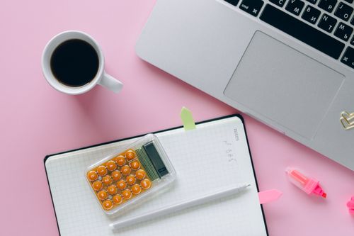 Free A vibrant flat lay workspace featuring a laptop, coffee, calculator, and notebook on a pink surface. Stock Photo