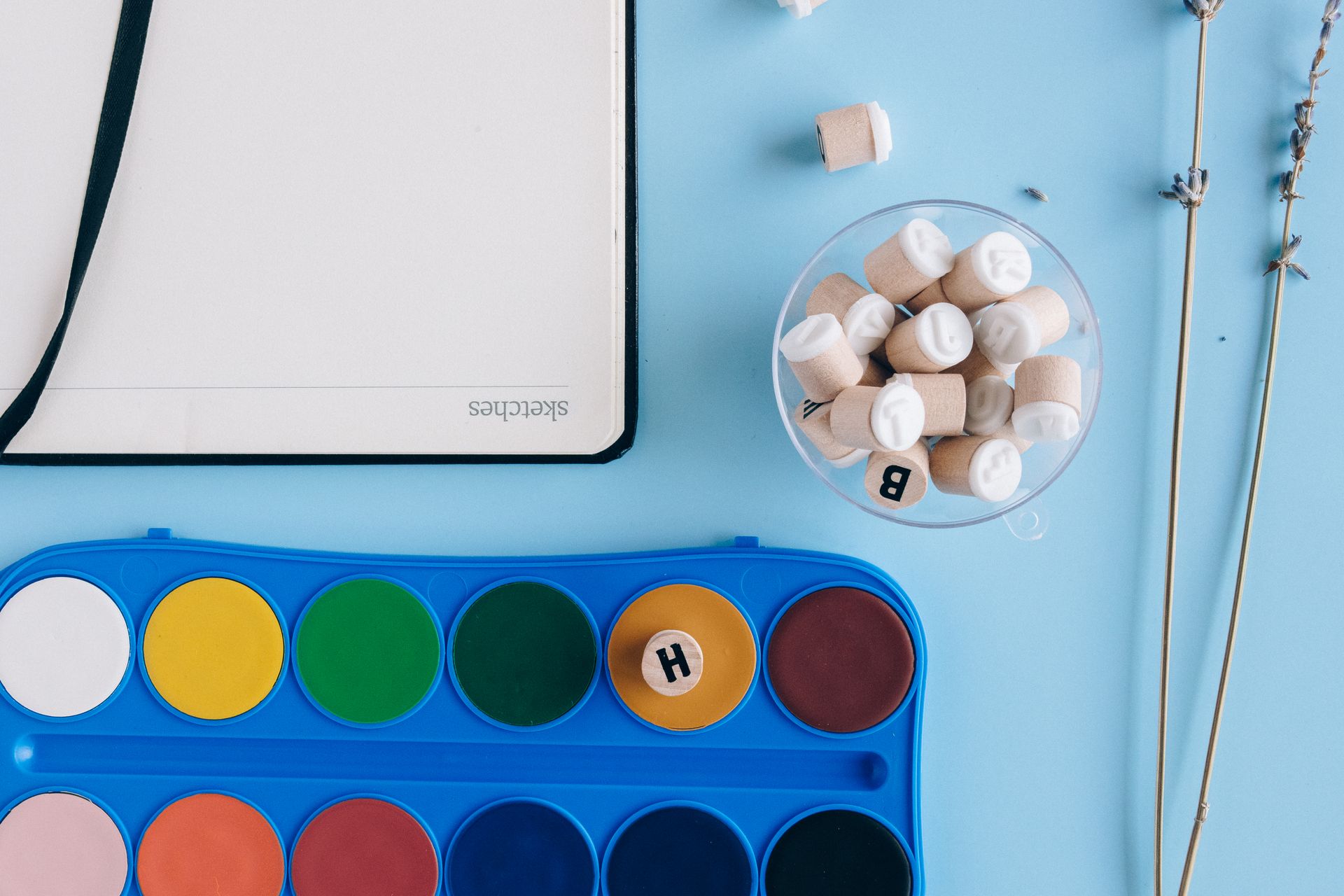 Flatlay of art supplies including watercolors and a notebook on a blue background.