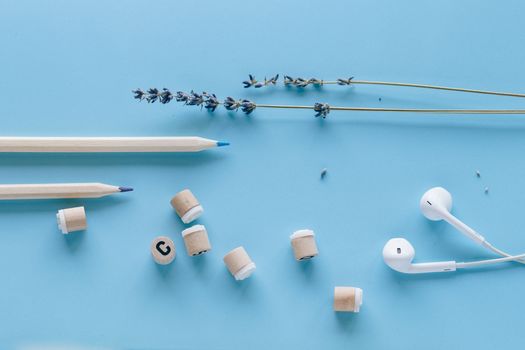 Artistic arrangement of pencils, lavender, and earphones on blue background for creative inspiration.