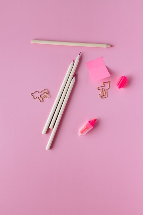 Free Top view of school supplies including pencils, paper clips, and sticky notes on a pink background. Stock Photo