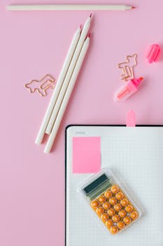 Vibrant office supplies and notebook on a pastel pink surface, perfect for workspace inspiration.