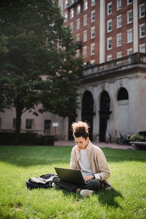 Ethnic man sitting on grass with netbook