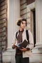 在大学大楼外，一位戴着耳机、手里拿着文件夹的年轻人显得富有洞察力
