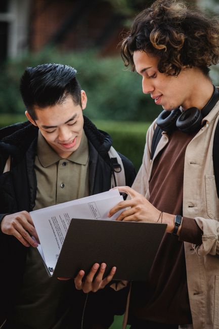 Young multiracial guys in casual clothes standing in street with folder and papers while having conversation in daytime Young multiracial guys in casual clothes standing in street with folder and papers while having conversation in daytime