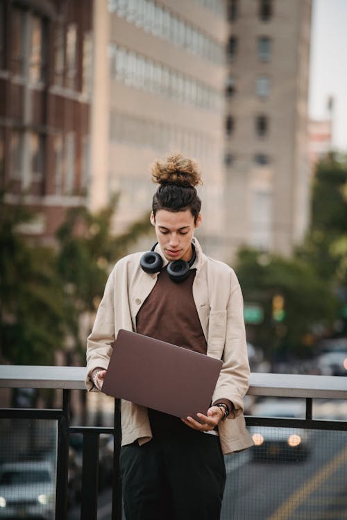 Ethnic guy standing near road and building with laptop
