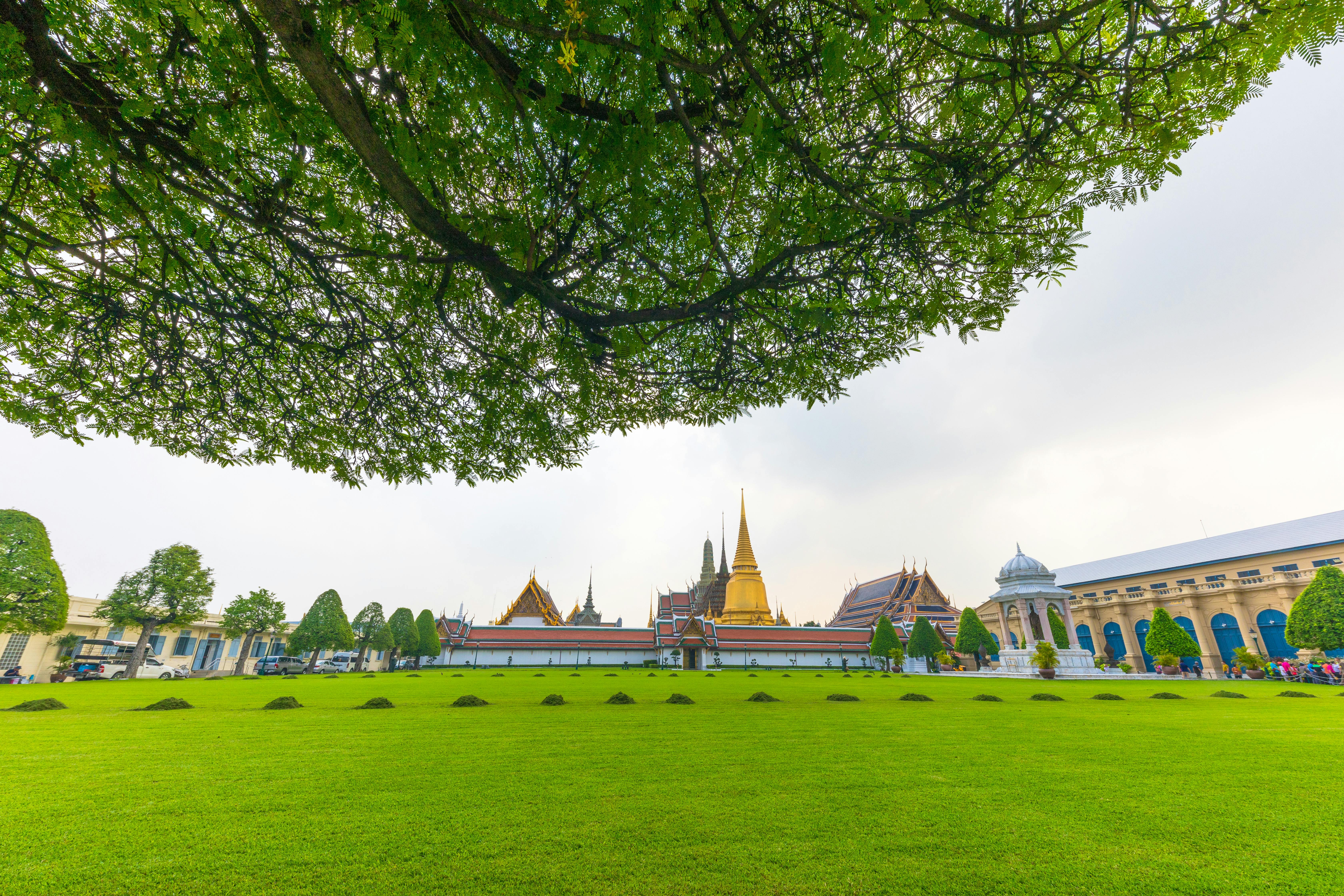 Lush garden view of the famous Grand Palace in Bangkok, Thailand, framed by trees.