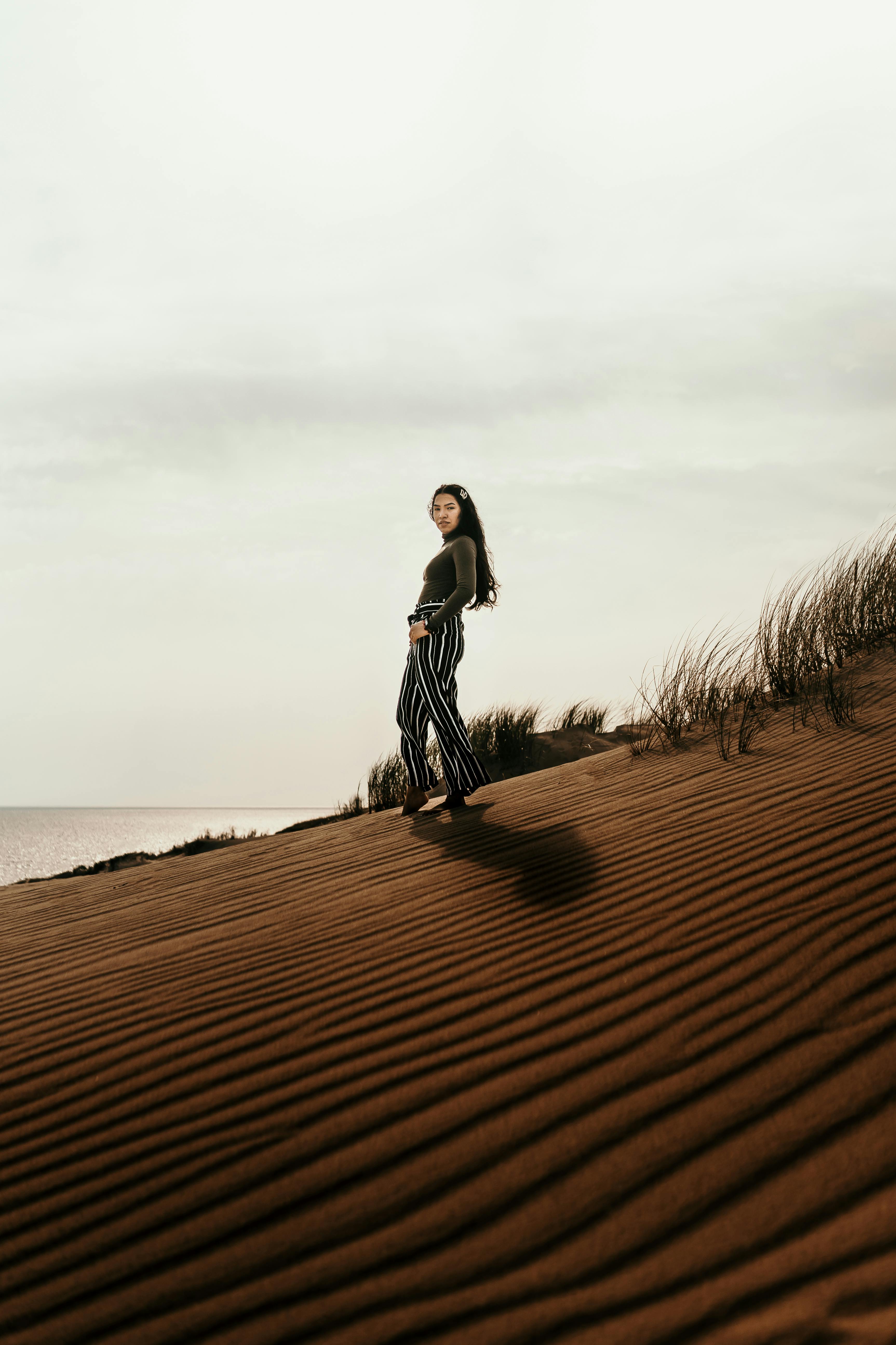 A woman stands gracefully on the picturesque sand dunes of Nida, Lithuania, under a tranquil sky.