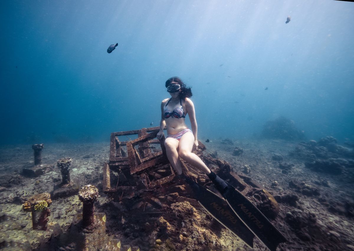 A freediver exploring a shipwreck underwater in Bali with sunlight coming down through the water