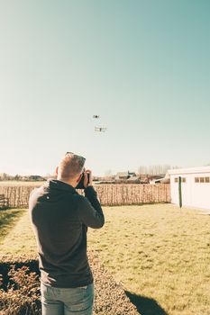 A man controls a flying drone in a bright and sunny open field setting.