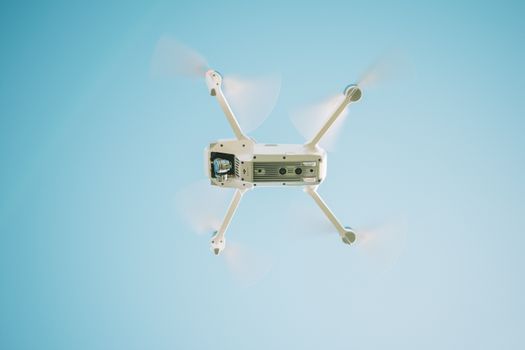 A sleek white drone flying under a clear blue sky, capturing aerial views.