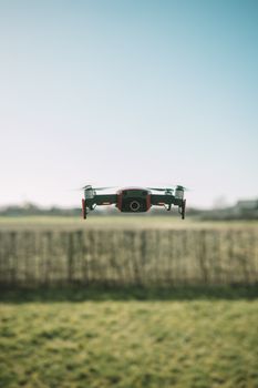 A drone flying over a grassy field on a sunny day with a clear blue sky in the background.
