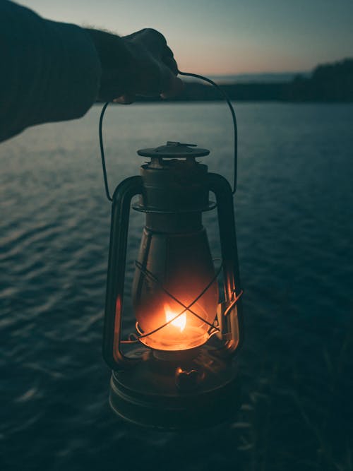 Person Holding a Black Lantern Near Body of Water 