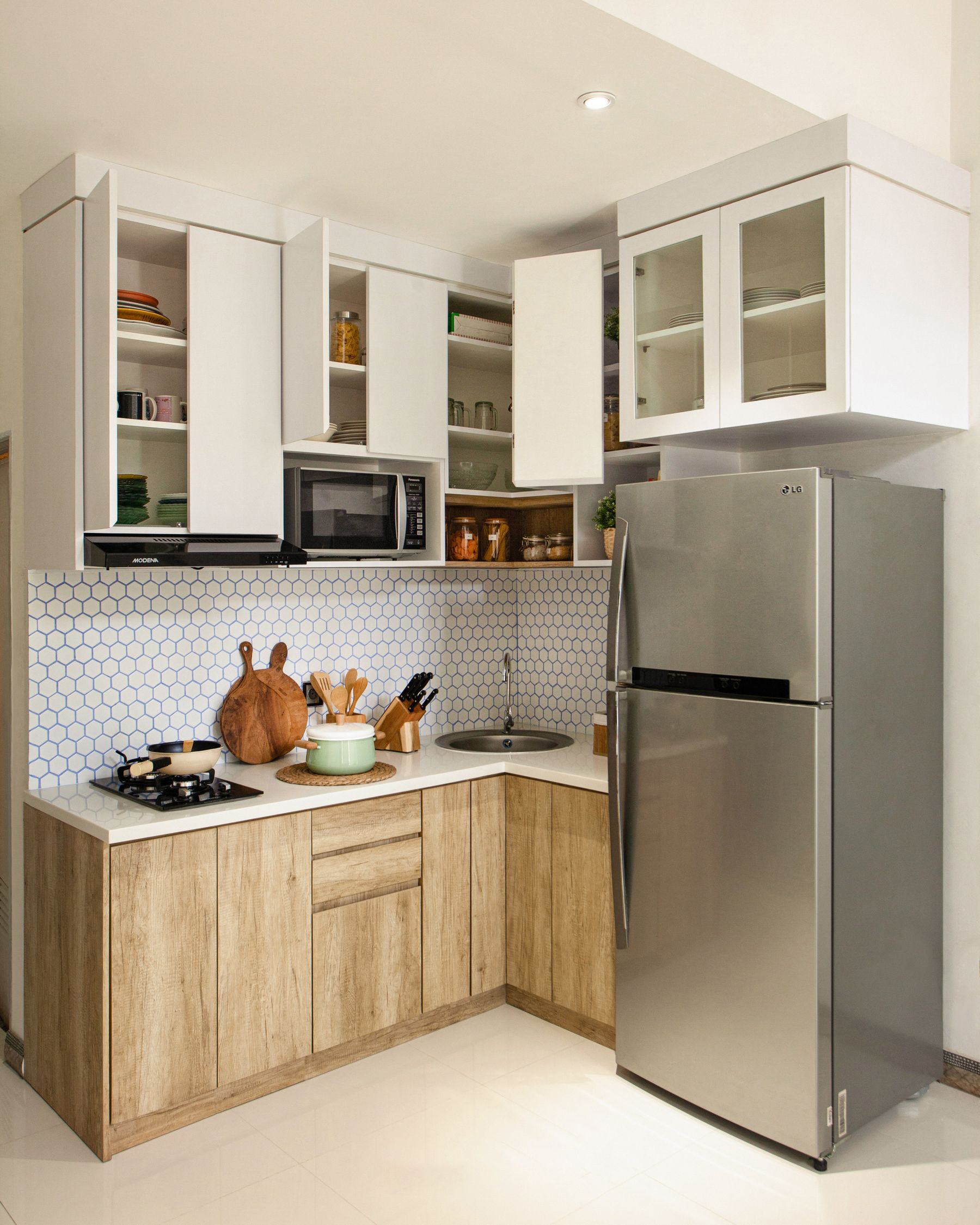 Compact corner kitchen with wood base cabinets, white upper storage and hexagonal tiles